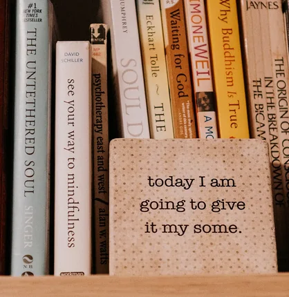 Books on a shelf beside a small sign reading “today I am going to give it my some”