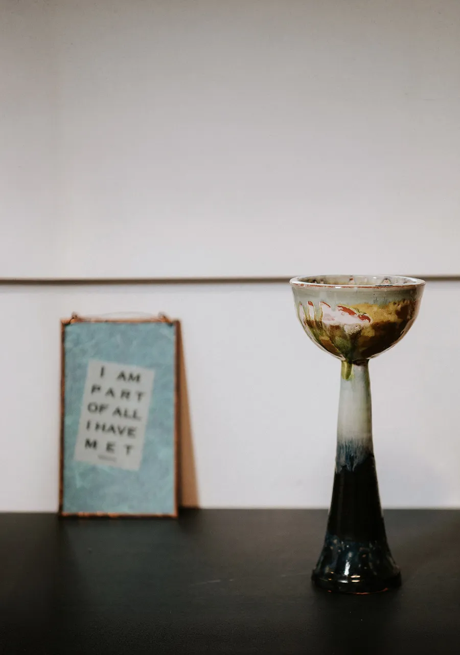 A handmade ceramic chalice beside a small framed card reading &ldquo;I am part of all I have met&rdquo;